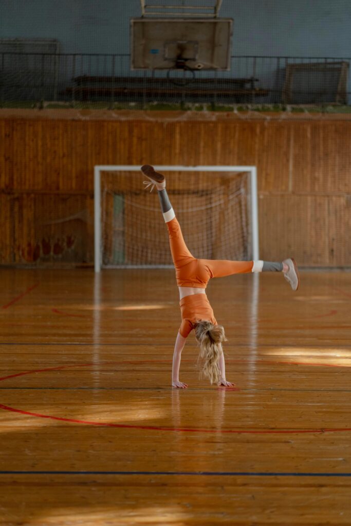 A young girl in orange attire performs a cartwheel on a gymnasium floor, showcasing her gymnastics skills.